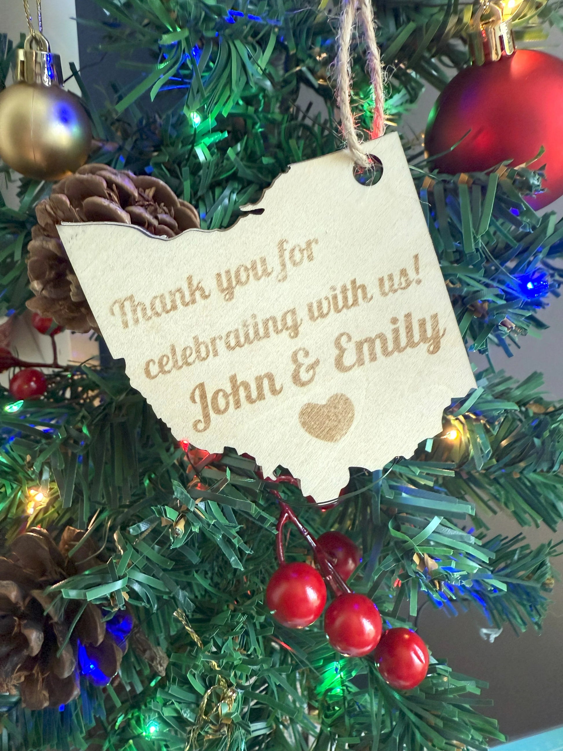 Christmas ornament with a tag reading 'Thank you for celebrating with us! John & Emily' on a decorated tree.