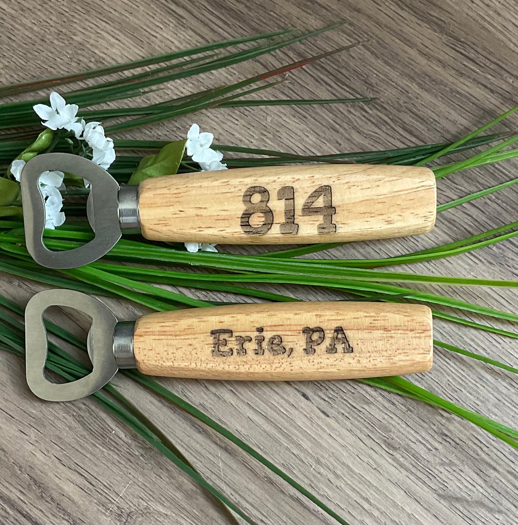 Two wooden bottle openers with engraved text on a wooden surface with greenery.